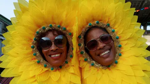 Reuters Two women, dressed as yellow flowers, smile at the camera, wearing sunglasses and petals