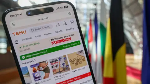 EPA Smartphone screen showing Temu website with flags in the background, at the headquarters of the European Council in Brussels.