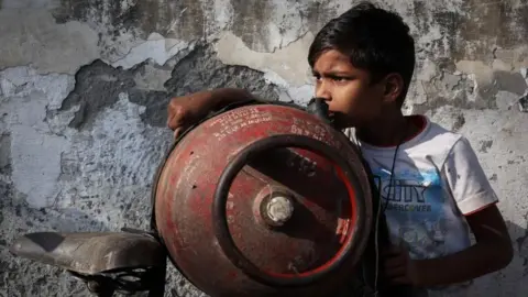 Reuters A boy stands next to an empty LPG cylinder tied to a bicycle as he waits outside a gas agency