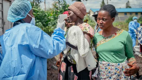 Anadolu via Getty Images A health worker in blue scrubs and protective gear carries out temperature screening for travellers at the Kanyaruchinya checkpoint near Goma, eastern DR Congo. Photo: 25 May 2026