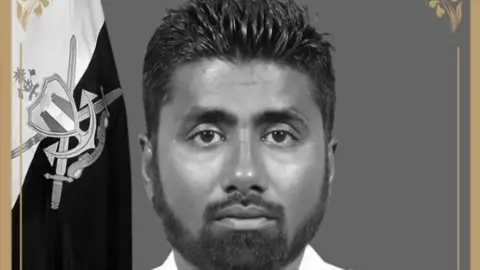 Maldives government Maldivian diver Mohamed Mahdhee, with dark hair and beard, looks towards the camera. There is a flag behind him.