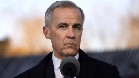 EPA Canadian Prime Minister Mark Carney speaks during a press conference in Beijing, China, 16 January 2026. He is seen standing in front of a microphone, and is wearing a black coat over a suit and tie. He has a serious expression on his face. He has short black and grey hair that is parted to the left. 