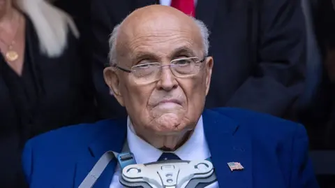 Getty Images Giuliani wearing a brace on his chest. He has a blue suit and glasses and looks towards the camera