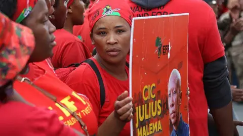 AFP via Getty Images An EFF supporter is seen in the party's signature red regalia holding up a poster of leader Julius Malema