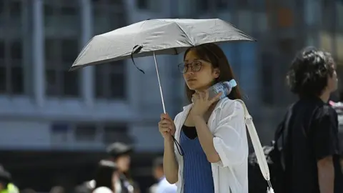 David Mareuil/Anadolu via Getty Images A woman walking on the street shields herself with a parasol on June 17, 2025, in Tokyo, Japan.