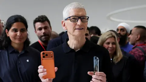 Reuters A man holds an iPhone with a crowd of people behind him.