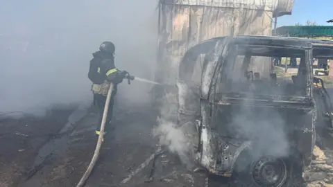 Reuters Firefighter trains hose on burnt-out vehicle in Kharkiv region of Ukraine on 7 May following Russian drone strike