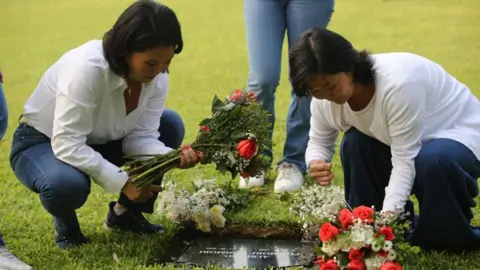 GERMAN FALCON/EPA/Shutterstock Presidential candidate Keiko Fujimori (left) visits the grave of her father, former Peruvian President Alberto Fujimori, at the Campo Fe Cemetery accompanied by her sister Sachi (R), in Lima, Peru, 12 April 2026.
Both sisters are wearing jeans and white long-sleeved T-shirts. They are laying flowers on the grave. 