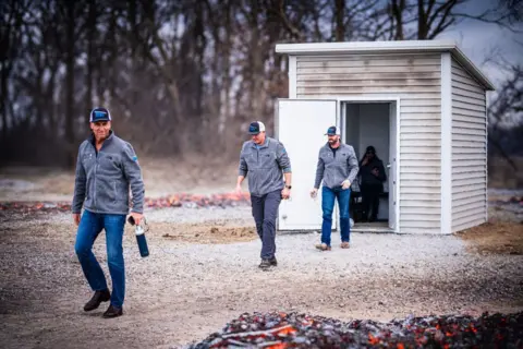 Fort / submitted photo Men carrying fire extinguishers leave an intact shed that is surrounded by smoldering wood