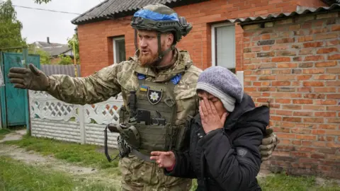 Reuters Ukrainian soldier in uniform helping a woman in tears evacuate from village in Kharkiv
