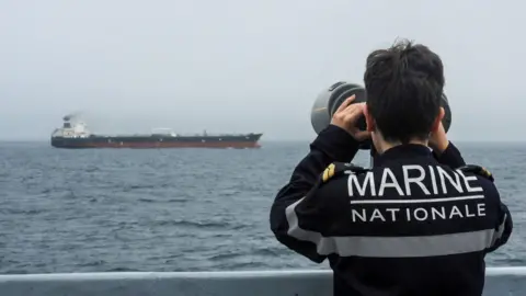 Reuters A French Navy officer wearing a black uniform labelled Marine Nationale observes an alleged Russian oil tanker sailing in the Atlantic ocean.