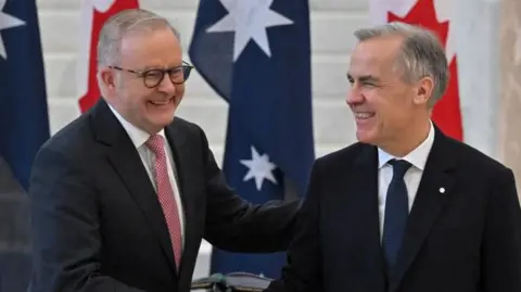AAP Two middle aged men with grey hair and wearing dark suits smile in front of the Australian and Canadian flags.