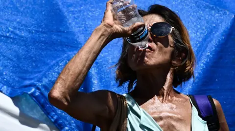 AFP A woman drinks water while cooling down in a tent in Phoenix's largest homeless encampment, amid the city's worst heat wave on record on 25 July , 2023