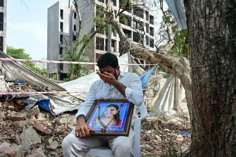 AFP via Getty Images A man breaks down while holding a portrait of his relative, who died in the Air India Flight 171 crash last year, at the accident site in Ahmedabad on June 12, 2026. Families of those killed in last year's Air India plane crash gathered at the site on June 12 to mark the anniversary of the disaster, still awaiting answers about its cause. (Photo by Shammi MEHRA / AFP via Getty Images)