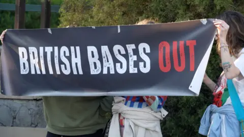 Jessica Parker/BBC Three people standing behind a black sign they are holding up that reads white and red: 