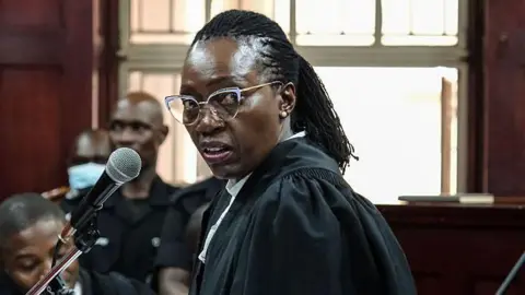 Getty Images Martha Karua in a black lawyer robe and glasses makes her submission during a court session in Kampala