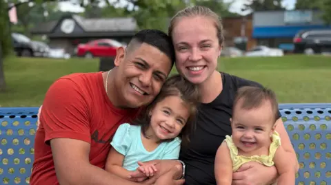 Submitted by Janie Pérez The Pérez family sit on a park bench - mother, father and two little girls 