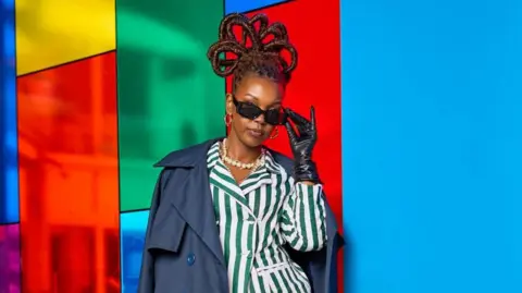 Zia Bett Zia Bett poses wearing sunglasses, a striped suit and a blue jacket