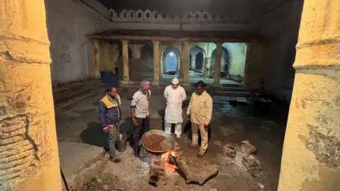 Aman/BBC Four men stand around a big plate of kebabs which are being cooked on a traditional wood fired stove at the Shahi Bawarchikhana inside Chota Imambara in Lucknow.