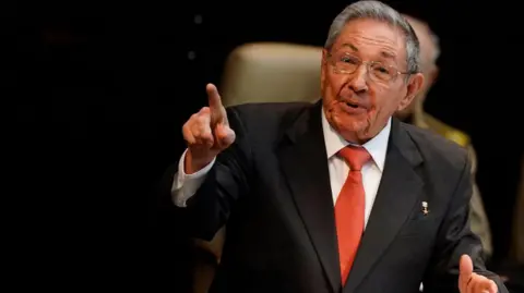 AP via Getty Images Raul Castro wearing a suit with red tie and wire framed glasses, and pointing a finger while speaking