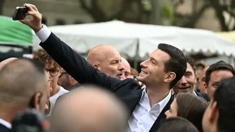 AFP via Getty Images Rassemblement National (RN) president Jordan Bardella takes a selfie during a visit in Beaucaire in France