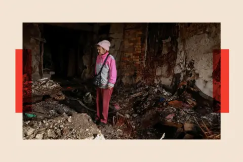 Reuters A woman dressed in pink inspects the ruins after a Russian attack on Ukraine