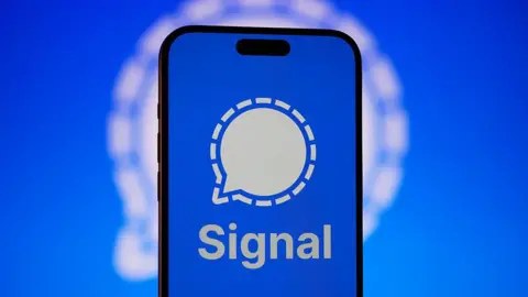 Getty Images Signal app logo displayed on a smartphone against a blue background, with a larger, blurred version of the logo behind it.