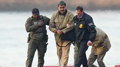 Getty Images Nicolas Maduro is seen in handcuffs after landing at a Manhattan helipad, escorted by heavily armed Federal agents as they make their way into an armored car en route to a Federal courthouse in Manhattan on 5 January 2026 in New York City. 