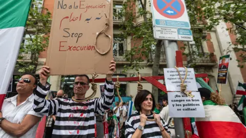 Getty Images Two people dressed as hanged prisoners, with painted blood on their faces and nooses around their necks, take part in a protest against executions in Iran by opponents of the Islamic Republic, outside the US embassy of Madrid, Spain (11 April 2026)