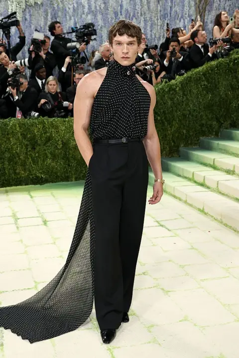 Getty Images Connor Storrie wears a black dotted halter top with a long train flowing from the neck.