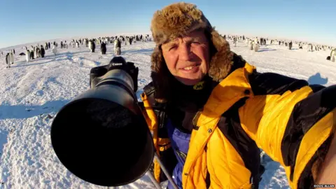 Doug Allan a man in a yellow jacket and furry hat with a large camera 