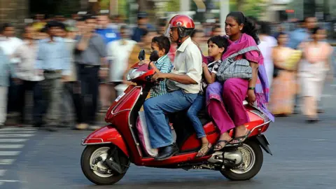 Getty Images A family of four - father, mother and two children, travel on a scooter in India