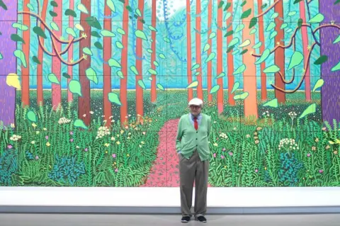 Getty Images David Hockney in front of 'The Arrival of Spring in Woldgate, East Yorkshire' at the Pompidou Centre in Paris. The painting is huge and of a countryside scene.