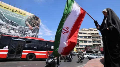 Anadolu via Getty Images A woman waves Iran's national flag in front of a giant billboard 
