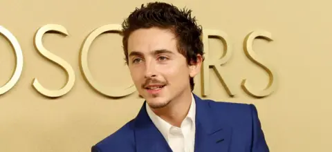 Getty Images Timothée Chalamet attends the 98th Oscar Nominees Luncheon at The Beverly Hilton on February 10, 2026 in Beverly Hills, California. He is wearing a white shirt and blue jacket.