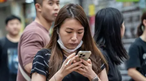 Getty Images A woman holding a cigarette and looking at her phone in Hong Kong, China, on June 6, 2024