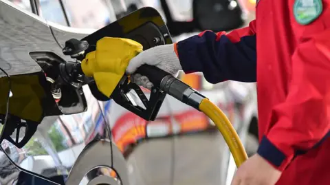 Costfoto/NurPhoto via Getty Images A person holds a gas pump and refuels a car at a petrol station in Fuyang City, Anhui Province, China, on April 7, 2026. 