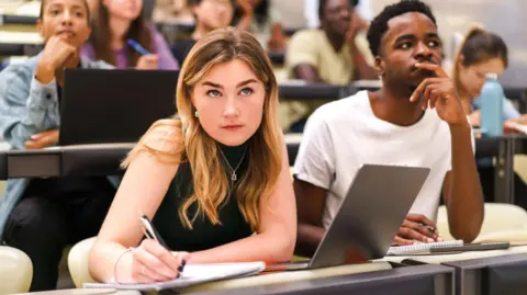 Getty Images A stock photo of students in a classroom, with one woman jotting in her notepad 