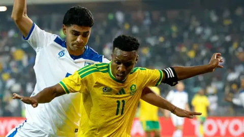AFP via Getty Images A South Africa player holds his arms out as he tries to stop a Nicaraguan player from coming up from behind him.