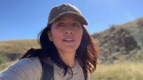 Find Melissa Mondragon Casias/Facebook A selfie of Melissa Casias. She has long brunette hair and is wearing a baseball cap and a backpack.