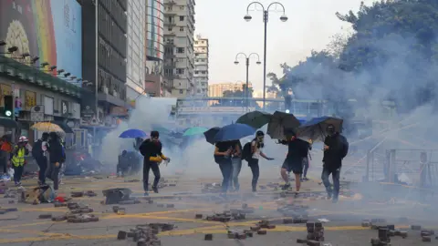 European Press Photo Agency Protestors, many holding umbrellas, run from police and security staff on a road in Hong Kong. There appears to be teargas. 