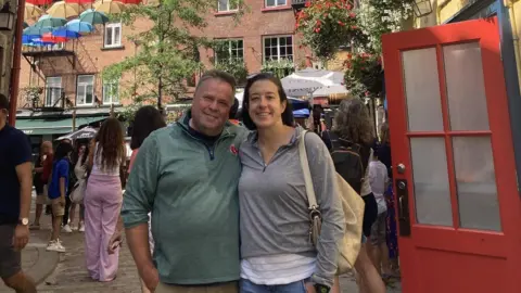 Submitted photo Joe Boucher and his wife stand in a busy brick-lined street, smiling and wearing zip-up sweatshirts