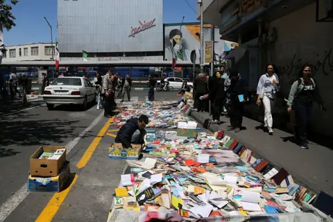 Getty Images A bookseller lays out hundreds of books by the side of a road in Tehran as people walk by