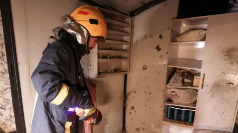 Getty Images An emergency services responder wearing a helment and reflective jacket stands in a hair salon damaged in a strike in the occupied West Bank.