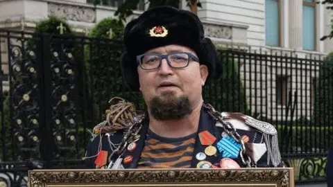 Facebook/Semyon Skrepetsky A man wearing an old-style Russian hat with a Soviet badge holds the top of a framed picture and wears a jacket crammed with medals