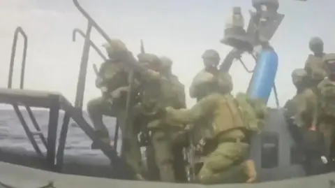 Global Sumud Flotilla/Handout via Reuters Video footage from the Global Sumud Flotilla showing armed commandos boarding a sailboat from a raiding craft in the Mediterranean, west of Cyprus (18 May 2026)