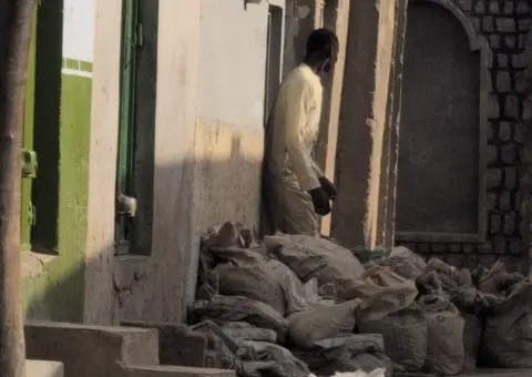 Mahmud Bashir A man standing in front of a home with several bags in front of the house