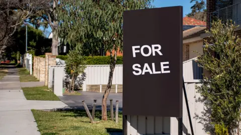 Getty A "For Sale" sign on a suburban street with with houses and gardens behind