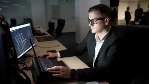 Man with glasses sat in the cyber operations centre in front of computer