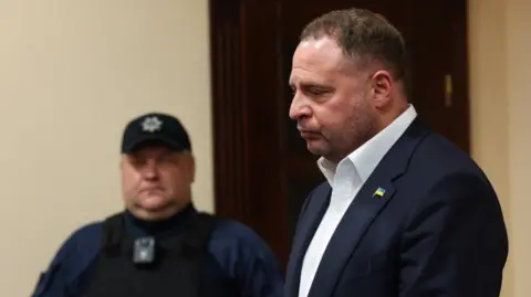 Reuters A man in a suit stands in court while a policeman looks on